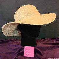 Side profile view showing the wide brim and woven raffia construction of the hat on a black mannequin head.