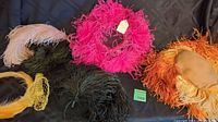 Full overview of the lot showing multiple feathered hats in colors orange, pink, black, yellow, and green, along with additional feathers and gloves