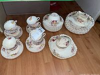 Full set of Copeland fine bone china arranged on wood floor showing cups, plates, covered sauce boat.