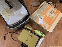 View of Moulinex Combine Jeannette hand mixer and vintage box, Rival waffle maker with chrome top, and yellow roaster oven on floor showing power cords and condition.