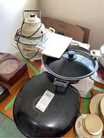 Assortment of kitchen electronics on a table including electric wok, black griddle, vacuum foodsaver, and convection cooker. Items are dusty and untested.