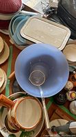 Photo showing several plastic bowls, including a large blue mixing bowl with a metal ladle inside, and a beige plastic rectangular container with lid, along with an orange-handled ceramic pot with floral design.