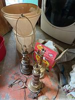 Four lamps including 3 metal bases and 1 brass base with attached cords, fabric lamp shades with damage, some bulbs in box Sani-Charms nearby