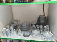 Full view of dish set showing stacked plates, cups, bowls, sugar bowl, creamer, and teapot.