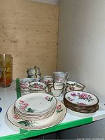 Assortment of tea cups, saucers, and plates with floral and gold trim arranged on a shelf. Some pieces stacked.