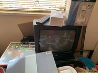 Overall view of the CRT TV, remote control on top, box for cordless phone standing behind TV, and vinyl record album partially visible with Christmas theme.