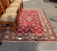 Full view of area rug with floral oriental design and border, showing red field and chair legs for scale.