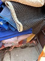 Stack of used moving blankets in black, blue, beige, and plaid.