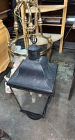 Photo of black metal lantern style post light showing glass panels, metal frame, and candle style light sockets inside.