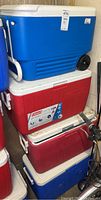 Four coolers stacked including blue and white Igloo cooler on top and red and blue Coleman chest coolers below.