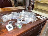 Overview of multiple small bags containing assorted costume jewelry including earrings and pins on wooden table.