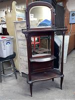 Front view of the wooden curio stand showing arched top mirror, rectangular lower mirror, decorative railing, and shelves