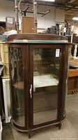 Full view of the vintage wood frame, glass side, door and shelves curio cabinet. Shows the cabinet's bay or oval-shaped glass door and sides with wood frame.