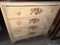 Front view of painted wood dresser showing all four drawers with floral applique and round wooden knobs with carved details.