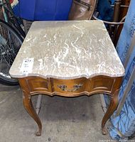 Front view of wood end table with faux marble top and one drawer with metal handle, showing wear.