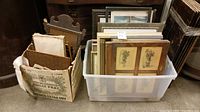 View of plastic and cardboard boxes filled with various framed photos and art prints.