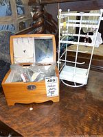 Photo of a wood finish jewelry box with mirror in the lid, several compartments inside, and a white metal jewelry stand holding earrings on a wooden surface.