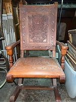 Front view of wooden rocking chair with carved Aztec design on backrest and seat, showing overall wear and discoloration.