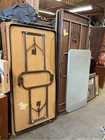 Photo showing five folding tables stacked vertically; frames and press board tops visible with signs of wear and scratches.