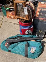 Photo showing vintage wooden tennis rackets inside a blue and red golf bag along with a green duffel bag on the ground.