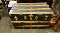Front view of the green vintage steamer trunk with metal clasps and wooden slats.