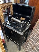 Full view of the Dictaphone shaving machine inside black wooden floor model case with open lid, showing the mechanical components on top.