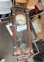 Full view of wood framed pendulum wall clock with visible pendulum and taped areas indicating damage.