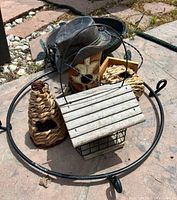 Photo of various decorative bird feeders including wooden, woven and a rustic metal feeder with a hat design inside a circular metal frame on a concrete surface.