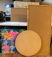 Photo showing multiple rectangular and round bulletin boards, a colorful floral painting, and fabric-covered sewing boxes.