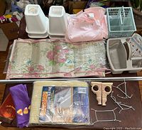 White plastic bed risers, pink hanging shoe organizer, floral patterned shower curtain or mat, small storage bins, metal hooks, and other organizational household items.