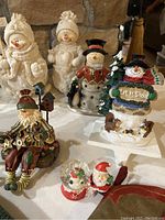 Photo of snowman and Santa figurines including snowmen in scarves and hats, Santa figure and 'Let It Snow' decoration with tree and dogs.