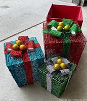 Colorful large wire mesh gift boxes with bows and gold ball ornaments, blue, red, and green, stacked together.