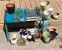 Overall lot showing green metal garden bench with various garden pots and planters arranged around it outdoors on a patio. Includes ceramic, plastic pots, and gardening accessories.