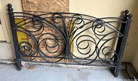Black metal headboard showing full piece with ornamental scrollwork and round finial corner posts.