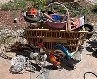 Full lot overview showing old chicken crate, three metal rooster statues, pink basket with garden tools, and sign.