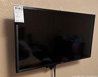 Samsung flat screen TV mounted on wall with label showing lot number and notes.