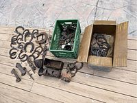 Top view of collection showing horseshoes arranged on floor, and cardboard box and green crate filled with assorted metal pieces and horseshoes, along with a variety of rusty garden tool parts.