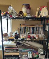 Shows 3 metal wire shelves with woodworking and craft supplies including books, paint, twine, and craft papers.