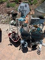 Full view of assorted yard decor including metal wall plaques, garden stakes, birdhouses, and statues on a stone ground outdoor setting.