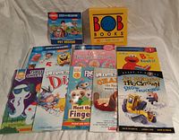Photo of multiple early reader books laid out, showing colorful covers, including boxed Bob Books set and various paperback titles.