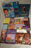 Photo showing the full lot of kids books spread out, including Dora and Friends projector and storybook, Peppa Pig book, and various other children's storybooks.