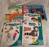 Photo showing front covers of assorted Kindergarten workbooks including Math, Reading, Writing Readiness, TinkerActive Math, First Grade Super Scholar, Key Words to Reading, and a French workbook titled 'Le Canada'