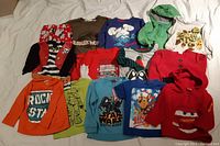 Front view of assorted boys shirts, showing variety of colors, prints, and styles including a green hoodie, pirate vest shirt, and Star Wars shirt.