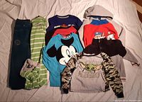 Photo showing all seven boys clothing items laid out, including pajamas, hoodies, and shirts in various colors and featuring characters such as Mickey Mouse, Baby Yoda, and Paw Patrol.