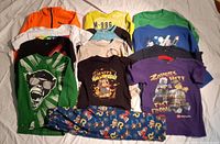 Front view of 10 boys size 5 clothing items, predominantly shirts with graphics or prints, arranged on surface