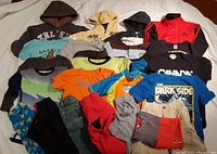 Photo of various boys clothing size 7 including hoodies, T-shirts, shorts, and pants arranged on a floor