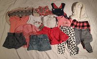 Full overview of all assorted baby girl clothing items including dresses, skirts, tops, leggings, and vest in various colors and patterns.