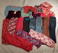 Overview of all clothing items including tops, jackets, pants, and leggings arranged on bed