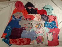 Photo shows an assortment of girls clothing size 4 including hats, tops, skirts, hoodies, and swimwear in various colors and designs.