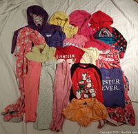 Top view of assorted girls size 4 clothing laid out showing a variety of colors including purple, red, pink, orange and patterns with graphical prints and text.